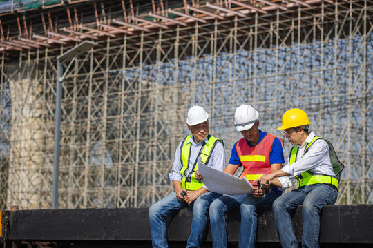 Team of Engineers and workers sitting on freight train reviewing blueprint at construction site, Construction team checking plan together on train car with bridge background