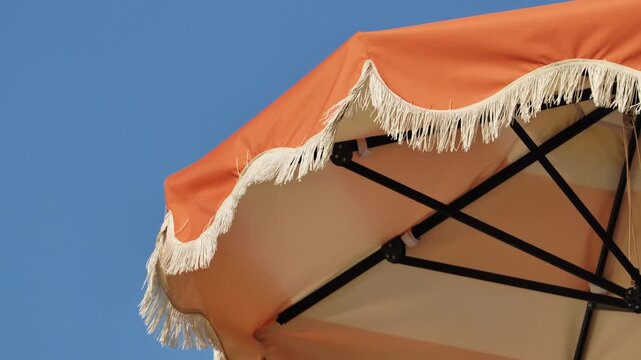 Orange beach umbrella providing shade with fringe detail against blue sky