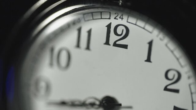 Macro close up of a white stopwatch face as the second hand ticks past the 12 at the top of the watch.