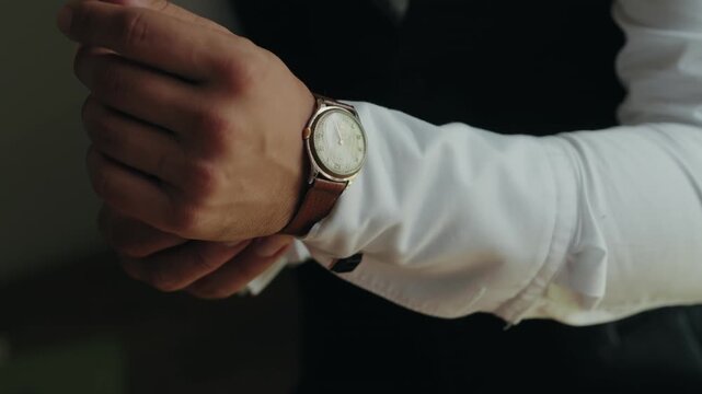 Hand adjusting a gold cased watch over a white shirt sleeve in low window light