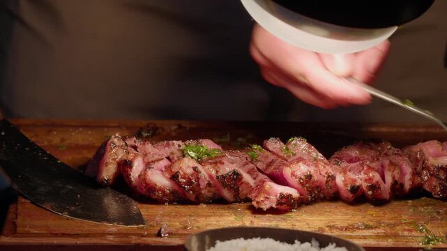 Hands adding chopped herbs then sea salt flakes over rested pink beef slices