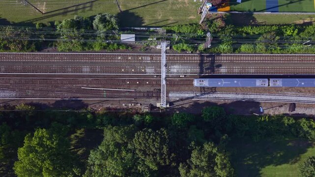 A top-down aerial footage of Long Island Rail Road train passing by from right to left. Highlighting commuter transportation and rail infrastructure on a sunny day. Camera remains stationary. .