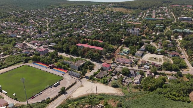 Aerial drone view over Hincesti, Moldova, showing a football stadium, residential neighborhoods, green urban landscape and the historic Manuc Bey Mansion in the background. Modern sports infrastructur