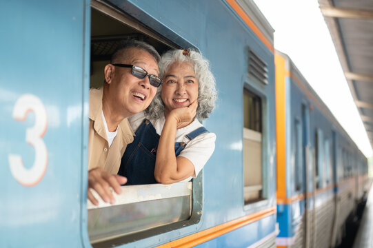 Asian senior couple smiling from a train window as they prepare to continue their journey.