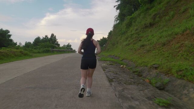 Asian woman jogging away along an empty mountain road during twilight in Mau Son, Vietnam, engaging in outdoor cardio fitness.