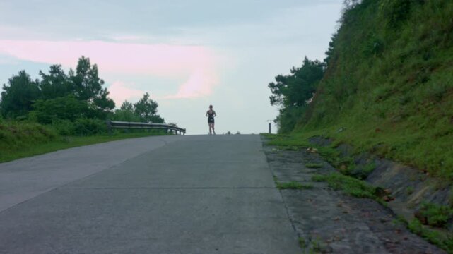 Female runner jogging uphill along a paved mountain road during sunset at Mau Son, Vietnam. Outdoor cardio endurance training and active travel lifestyle