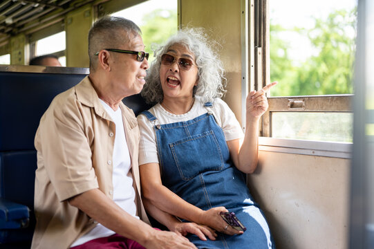 Asian senior elderly man and woman couple enjoying friendly conversation aboard a vintage train.
