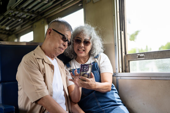 Asian senior elderly couple looking at smartphone together while enjoying their vintage train trip.