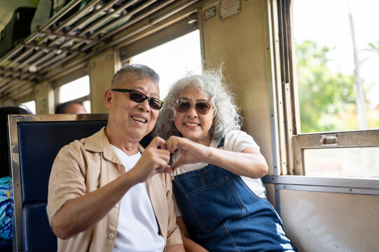 Asian senior elderly couple making a heart hand gesture together during their vintage train trip.