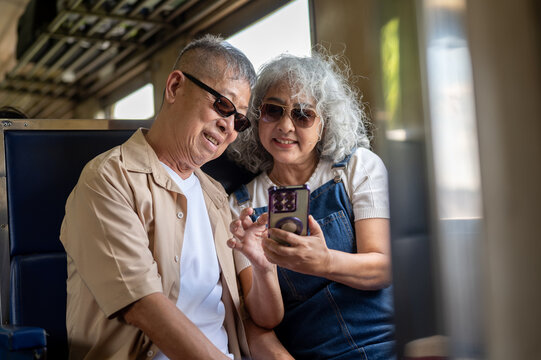 Asian senior couple looking at photos on a smartphone while traveling by train