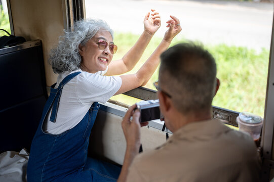 Asian senior couple traveling by train, elderly woman enjoying a journey while husband photographing