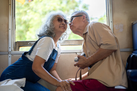 Asian senior elderly couple sharing a warm and tender kiss while seated together on a vintage train.