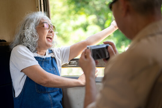 Asian senior woman laughing while photographing scenery during a train journey
