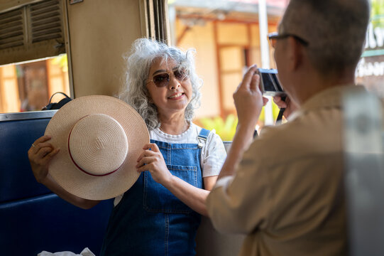 Asian senior elderly man taking a photo of his wife with camera inside a vintage train carriage.