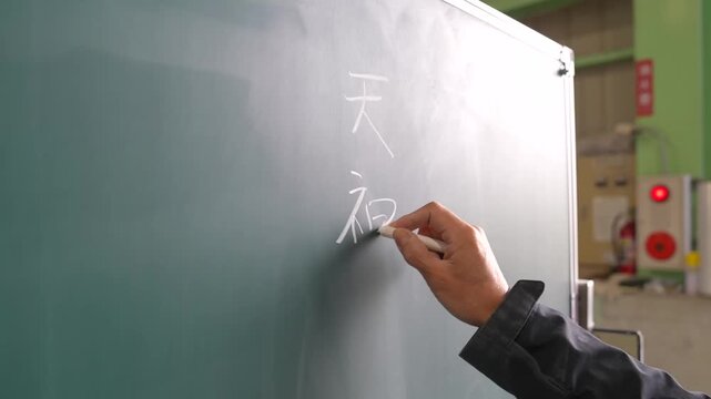 Hand writing Japanese kanji characters on a green blackboard with a white chalk stick at a chalk factory