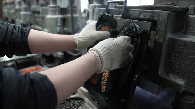 Worker lifting a freshly molded rubber outsole with an orange and black tread pattern out of a hot vulcanizing mold