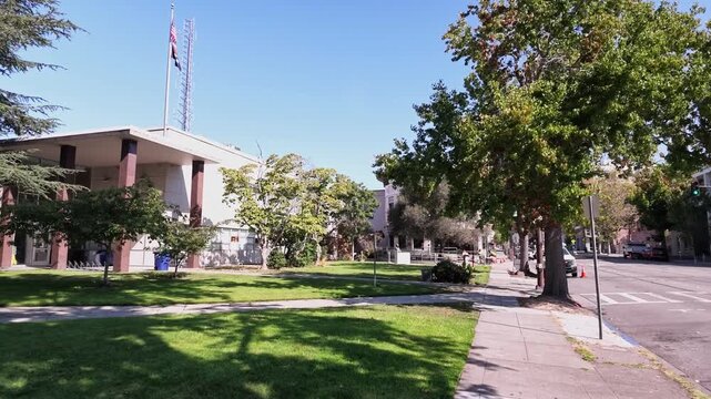 Sunny day view of the Court House and Ronald T. Tsukamoto Public Safety Building, home to the Berkeley Police Department and jail, featuring a grassy lawn, trees, and the street with passing cars