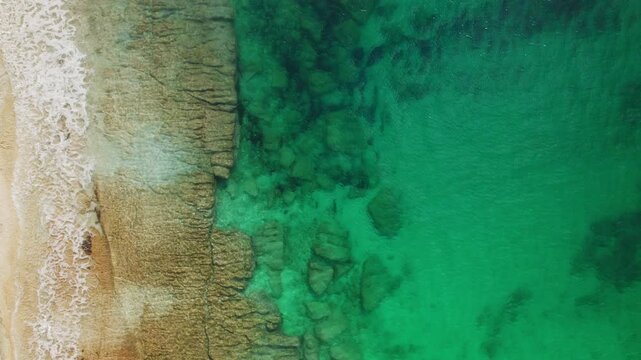 Aerial view of turquoise sea meeting sandy shore and underwater rock formations