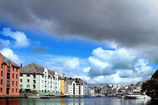 Beautiful waterfront Art Nouveau architecture and docked boats along Brosundet canal in Alesund, Norway. Contrast of blue sky and heavy storm clouds over the historic Brosundet canal.