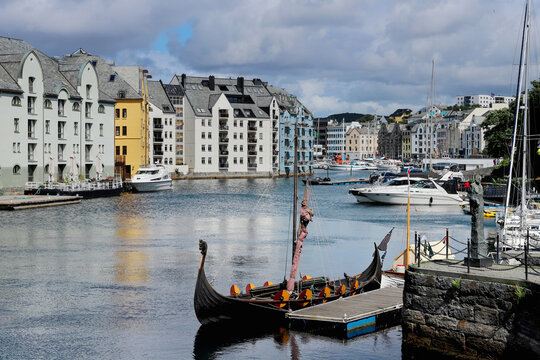Traditional viking ship replica docked in the Brosundet canal of Alesund Norway. Beautiful waterfront Art Nouveau heritage buildings and modern yachts along the canal in Alesund town.