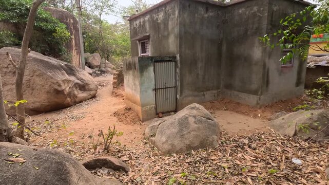 This stock footage captures a walking trail surrounded by large natural granite rock formations, lush trees, and scattered dry foliage at the famous Mama Bhagne Pahar in Dubrajpur, Birbhum, Westbengal