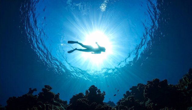Silhouette of swimmer freediving underwater in ocean with sunlight rays during tropical vacation