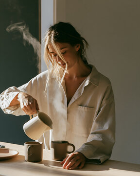 Woman pouring a hot drink from a stoneware jug into two mugs