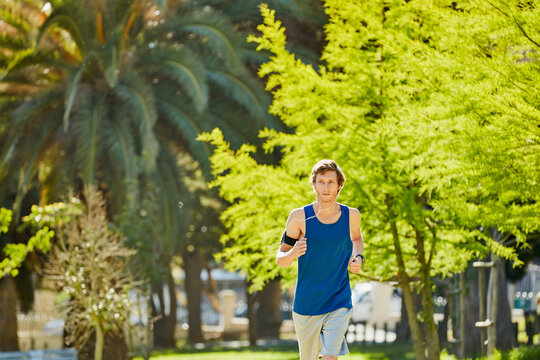Man, running and outdoor with earphones for fitness, exercise or streaming music with cardio wellness. Athlete, jogging or tech in park for radio, training tips podcast or challenge for heart health