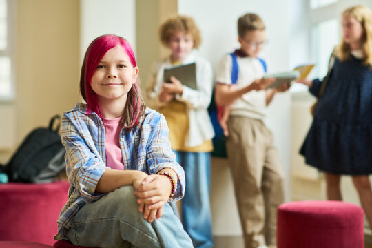 Portrait of Caucasian teenager girl smiling in school hallway with classmates in background. Image represents youth individuality and is suitable for K-12 education marketing