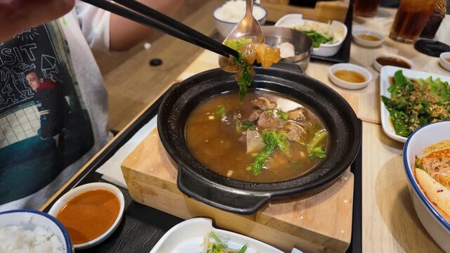 Person Eating Thai Beef Soup in Clay Pot with Chopsticks