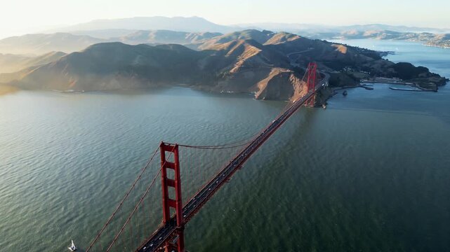 Aerial view of golden gate bridge with traffic flowing over suspension structure and sausalito hills in background.