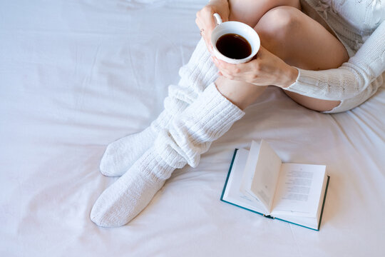 Young caucasian woman holding a porcelain cup of black coffee beside an open book on a bed, fits morning ritual, cafe and slow living content.