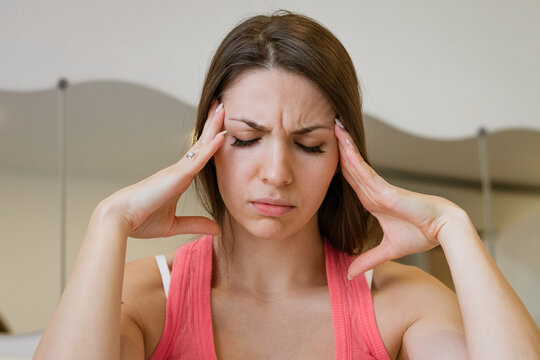 Close up portrait of a young caucasian woman suffering a headache with a frown and hands on her temples, for migraine, pain relief and head massage content.
