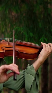 Woman playing violin in a tranquil forest, graceful hands guiding the bow across warm wooden strings, creating soulful music amid lush green woodland surroundings