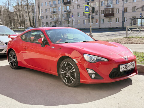 Bright red Toyota 86 sport coupe car parked on a city street. Modern Japanese automobile representing JDM car culture, featuring stylish dual-tone alloy wheels and sleek black exterior design details.