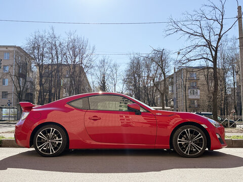 Bright red Toyota 86 sport coupe car parked on a city street. Modern Japanese automobile representing JDM car culture, featuring stylish dual-tone alloy wheels and sleek black exterior design details.