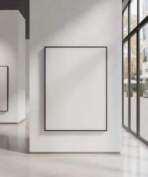 Black frame poster mockup hanging on white wall in art gallery or modern building with large window