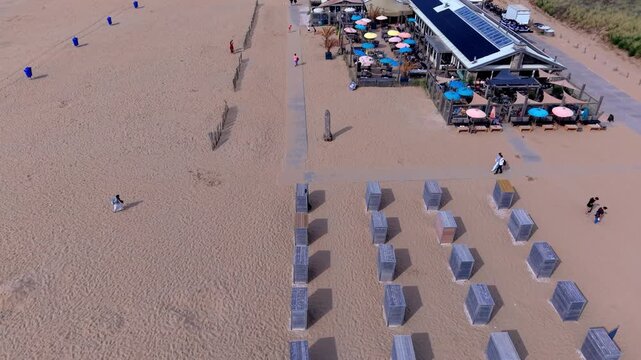 High angle horizontal aerial drone video clip of beach cabins, wooden huts, resort pavilion terrace, sand dunes, and beachgoers in Katwijk aan Zee beach, South Holland, Netherlands, West Europe