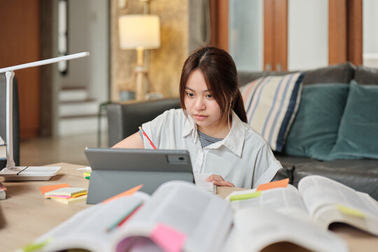 Asian teenage girl concentrates on online class, remote learning at home using tablet, writing and reading textbooks, self-study for back to school, Homeschooling, university education lifestyle.
