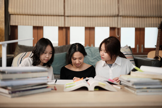 Three Asian teenage girls learning tutorials at home together, reading textbooks, writing notes, self-tutorial exams, preparing school homework, Homeschooling study, knowledge education lifestyle.