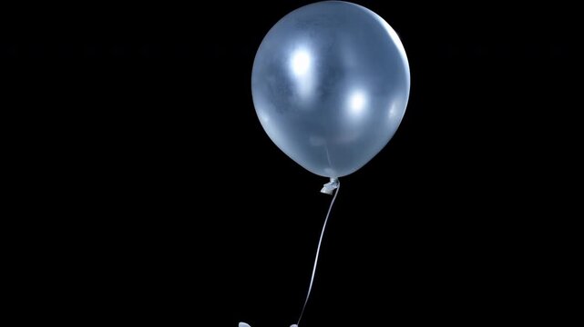 Hand holding blue balloon releases upward against dark background as round helium balloon rises slowly with thin string visible, creating isolated composition with soft reflections and calm movement