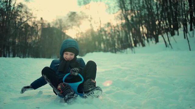 slow motion of happy little boy sledding on snow saucer downhill in winter, cheerful child enjoying outdoor fun in snowy wintertime 4k