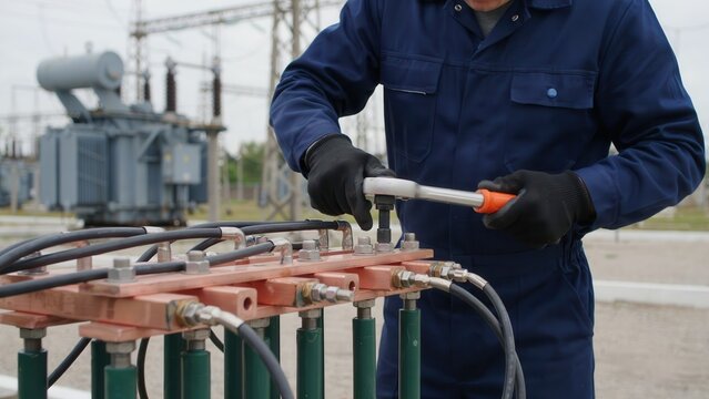 An electrical engineer repairs a high voltage transformer station using a socket wrench. Professional maintenance concept for energy industry infrastructure.