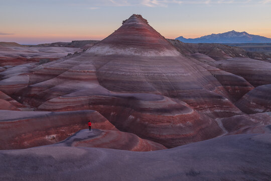 Aerial view shows peaceful hiker exploring colorful striped bentonite hill formation in utah desert landscape during scenic twilight
