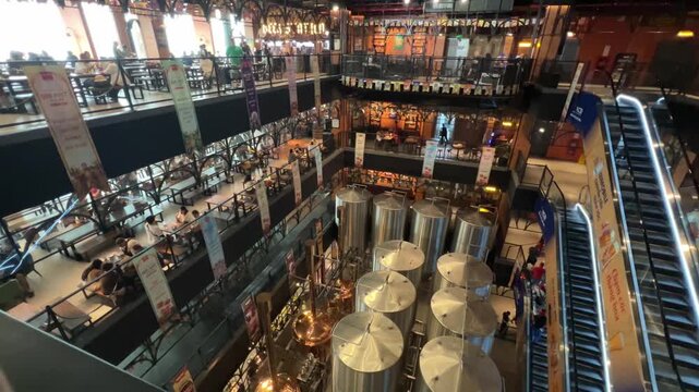 A wide interior view of the Bana Brew House at Ba Na Hills. The ground floor features large stainless steel and copper brewing vats, while others host patrons dining in a industrial-style atmosphere.