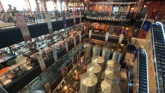A wide interior view of the Bana Brew House at Ba Na Hills. The ground floor features large stainless steel and copper brewing vats, while others host patrons dining in a industrial-style atmosphere.