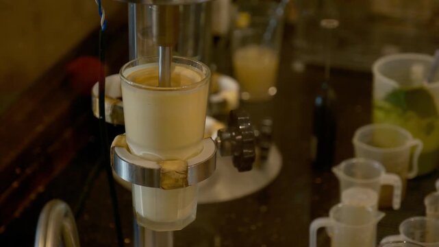 A close up view of a barista using a professional spindle drink mixer to blend a thick yellow egg and sweet condensed milk mixture inside a clear glass to create a creamy foam for some authentic drink