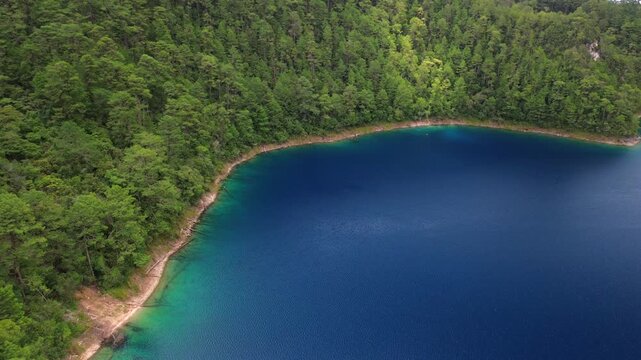 Static aerial drone wide shot of a deep blue lake shore with turquoise waters surrounded by pine forest at Montebello Lakes National Park in Chiapas, Mexico.