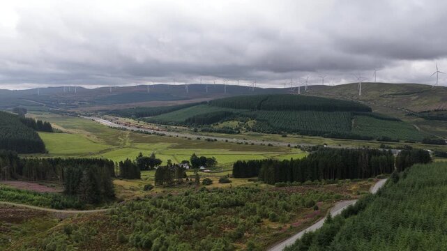Dramatic cloudy sky passing over a lush green valley with rolling hills, dense forests, and a large wind farm generating sustainable electrical power for a cleaner environment and future