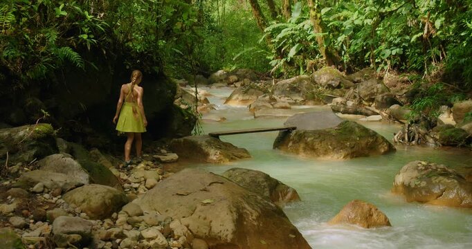 Woman walking by the edge of a turquoise river in tropical forest in Blue Falls Costa Rica